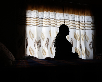 A woman, shown in shadow, sits posing in profile against the backdrop of a light white curtain with beige and brown designs.