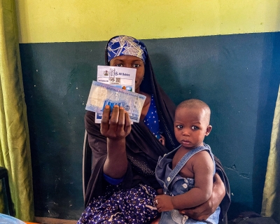 A mother holds up the cash incentive she received at the Farfaru clinic upon vaccinating her child. 