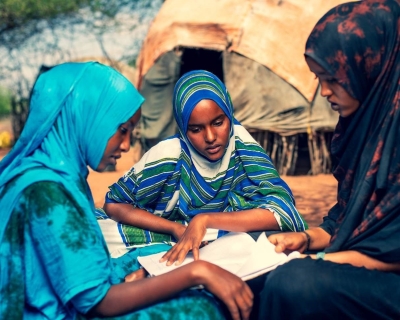 Three girls wearing colorful head scarves sit reading together.