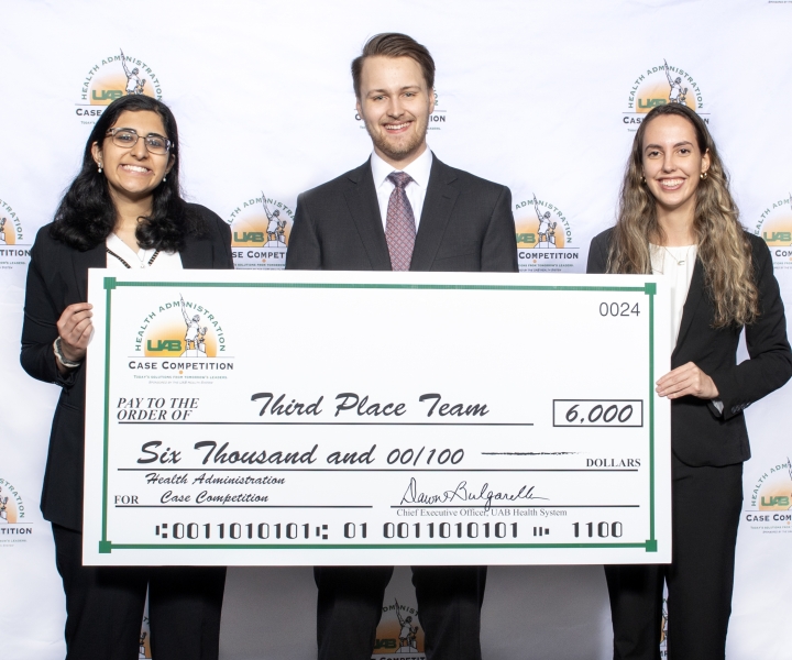 Three students wearing suits hold up a large check that reads $6,000