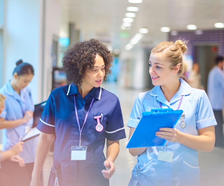 Two nurses walk through a hallway while looking at a clipboard