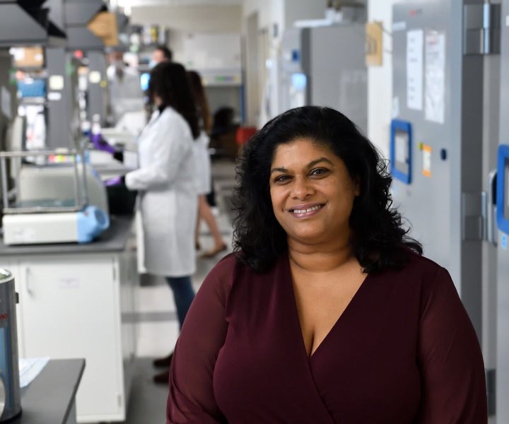 Ashani Weeraratna stands in her lab, with trainees working behind her