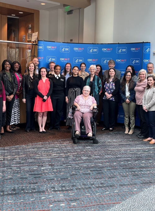 Group of alumni who currently work at CDC gathered with Dean MacKenzie for a posed photograph in front of a step and repeat.