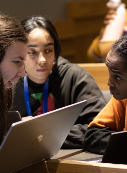 Three students in a classroom working together with a laptop open