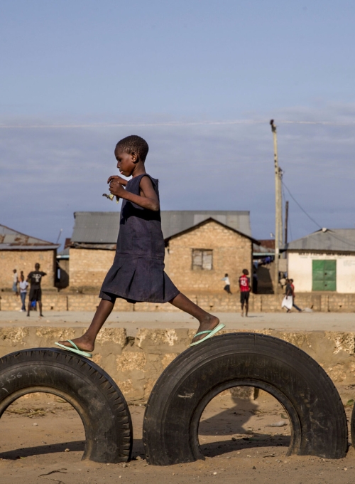 A young girl in Mombasa Kenya walking on top of discarded car tires