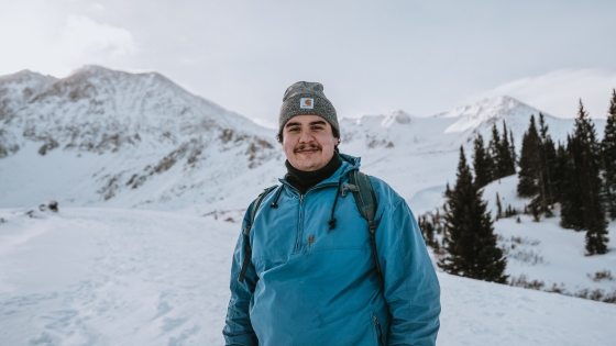 Young man in a teal coat and hat in a snowy landscape