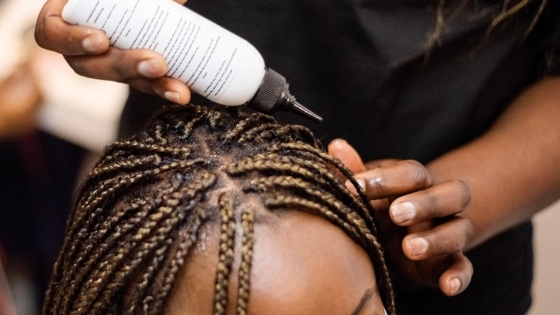 EHE-hairdressing-toxins Black hairdresser applying solution to a black female client's head.