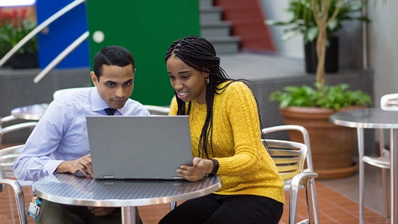 Two students in a college setting look at a laptop together 