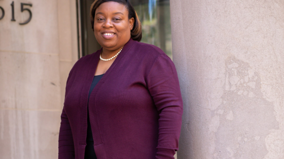 Tanjala S. Purnell stands on the steps with her back to a column, wearing a purple cardigan, black pants and shoes