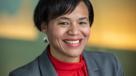 A headshot of department chair Keshia Pollack Porter. She smiles at the camera while wearing a red blouse under her grey suit jacket.