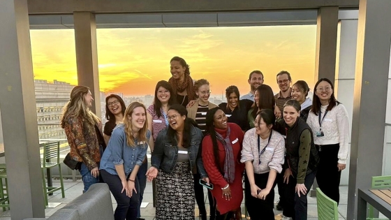 A small group of students gather on a balcony for a sunset photo.