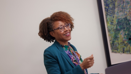 A female teacher standing behind a podium smiles at her classroom as she speaks.