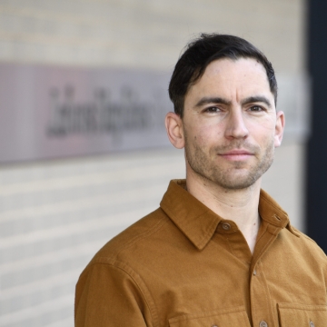 man standing outisde against wall the Johns Hopkins sign in background