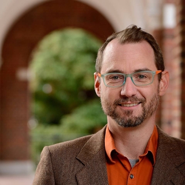 Ciaran Harman man wearing glasses, smiling, standing outside of building
