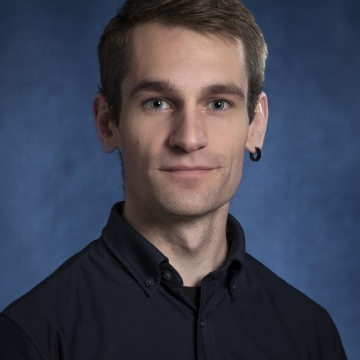 A white man in his early thirties with short brown hair and an earring in his left ear