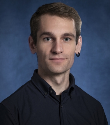 A white man in his early thirties with short brown hair and an earring in his left ear