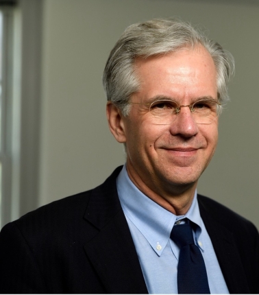 Headshot of HPM Distinguished Scholar Jeffrey Paul Michael wearing a suit jacket over a light blue button-up shirt with a black tie