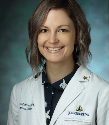 Headshot of HPM Assistant Professor Mariah Robertson wearing a white medical coat labeled with the the words Johns Hopkins 