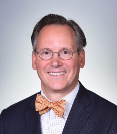 A headshot of a man wearing an orange bowtie and black suit jacket.
