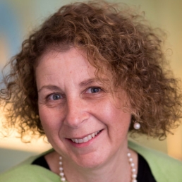 Woman with curly hair, wearing green sweater and pearls