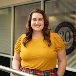 Katie Caviness-Crolley smiles for a photo in a yellow top and plaid skirt