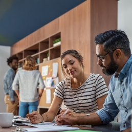 Two people sitting next to each other at a table, looking at a notebook