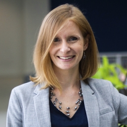 Valerie Sullivan smiles for a photo while wearing a gray blazer and navy blue top.