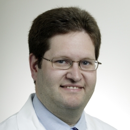 Elliott Haut, wearing his white coat and wire frame glasses, smiles for a photo in front of a white background.