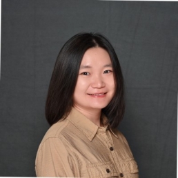 Chen Dun smiles for a photo in front a dark gray photo backdrop