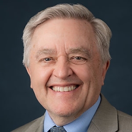 Dan Ford smiles for a photo in a tan suit and blue button up shirt.