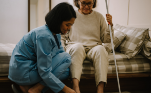 Image of middle aged woman helping an older woman out of bed