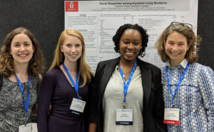 Four women standing side by side in front of presentation poster