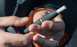 Hands of a man with a light complexion and black winter coat holding a black HTP heated tobacco product