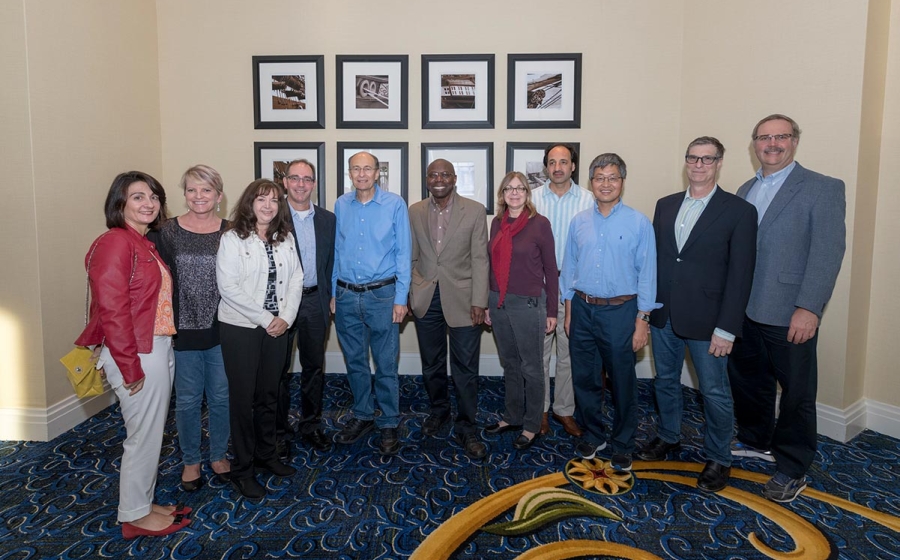 Roger McMacken stands surrounded by ten alumni he trained