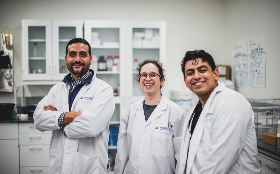Vito Rebecca and students in the Rebecca Lab Vito Rebecca and two students stand in lab wearing lab coats