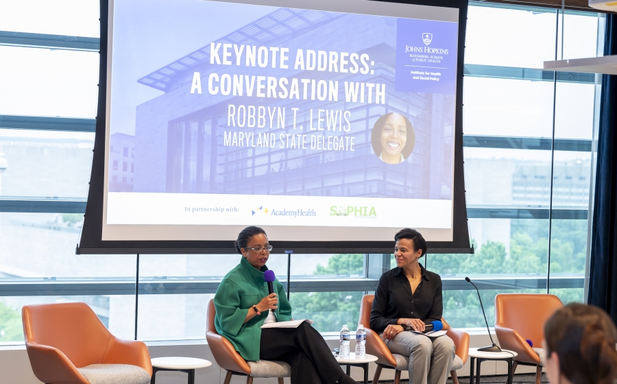 Department Chair Keshia Pollack Porter and Maryland State Delegate Robbyn T. Lewis seated at the front of the room in orange chairs with a projector screen behind them that reads Keynote Address: A Conversation with Robbyn T. Lewis.