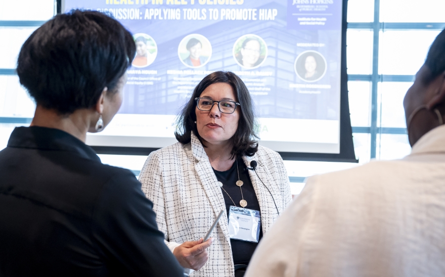 A woman is facing the camera and positioned between Department Chair Keshia Pollack Porter and a man, both of whom's backs are facing the camera. The woman is looking at Porter.