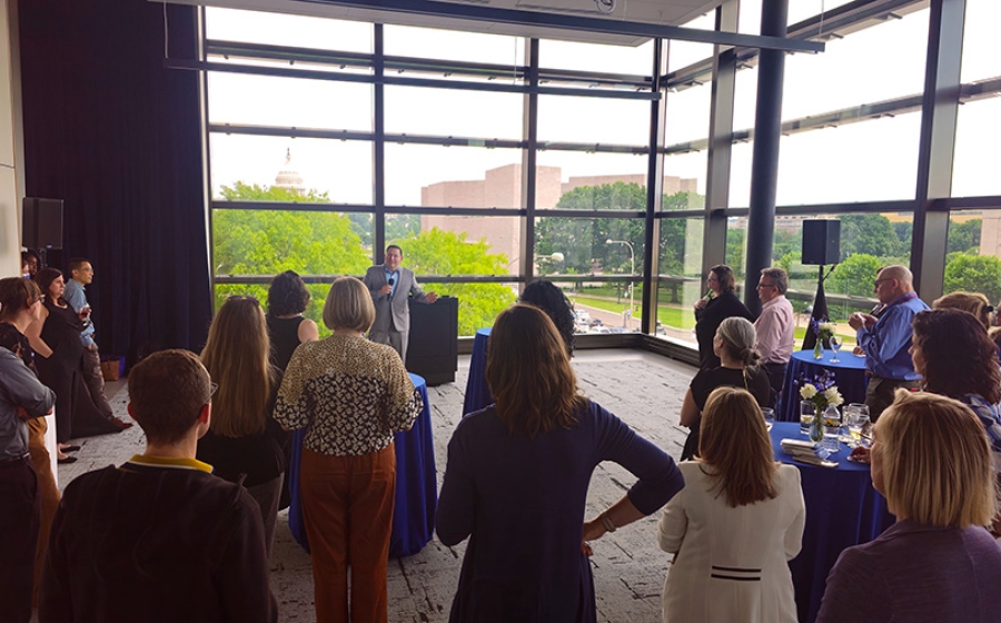 Man addressing room of adults with a window view of the Capitol