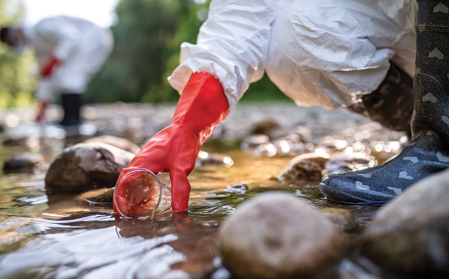 Collecting water samples Scientists in personal protective equipment collect water samples in cups from a stream