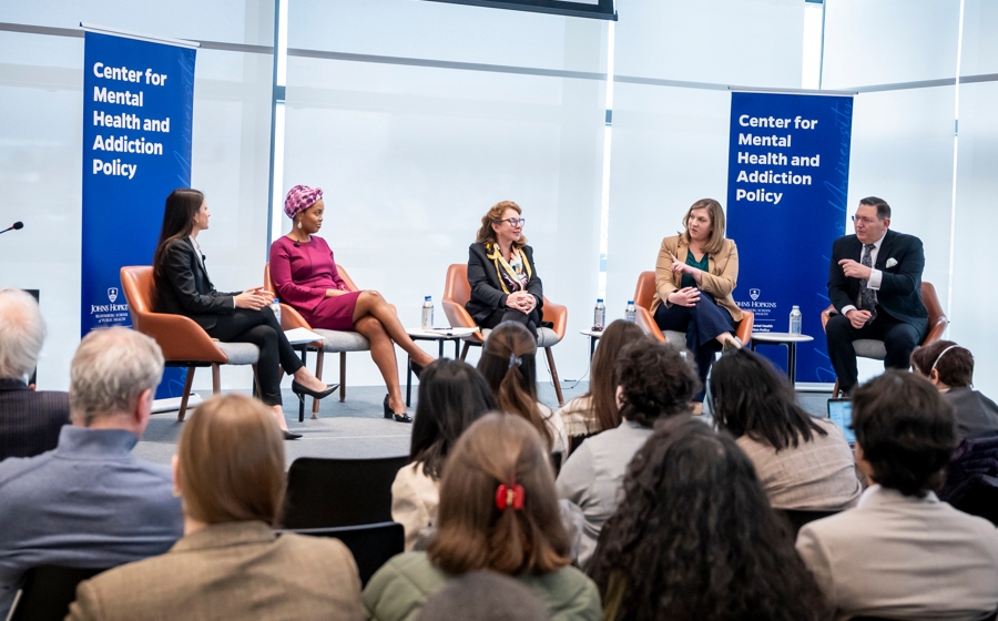 Five adults in business attire are seated on a stage. There is a banner that reads Center for Mental Health and Addiction Policy behind them.