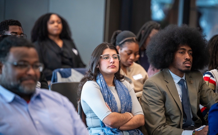 A few audience members are in focus among a crowd. They're wearing business attire.
