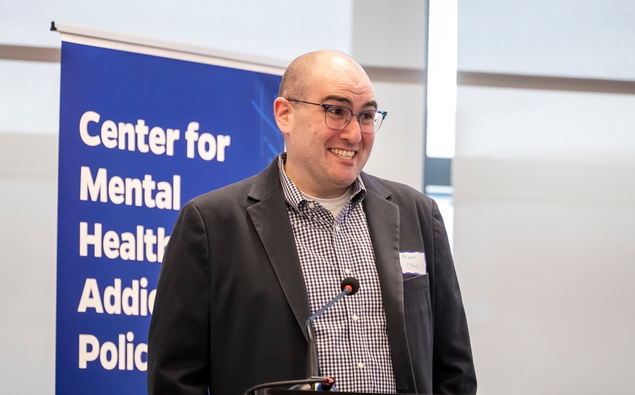 Man wearing suit behind a podium grins.
