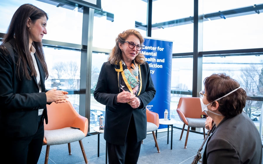 A red-haired woman speaks with a man who is wearing a mask.