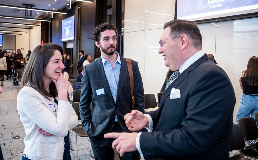 A man wearing a suit converses with two audience members.