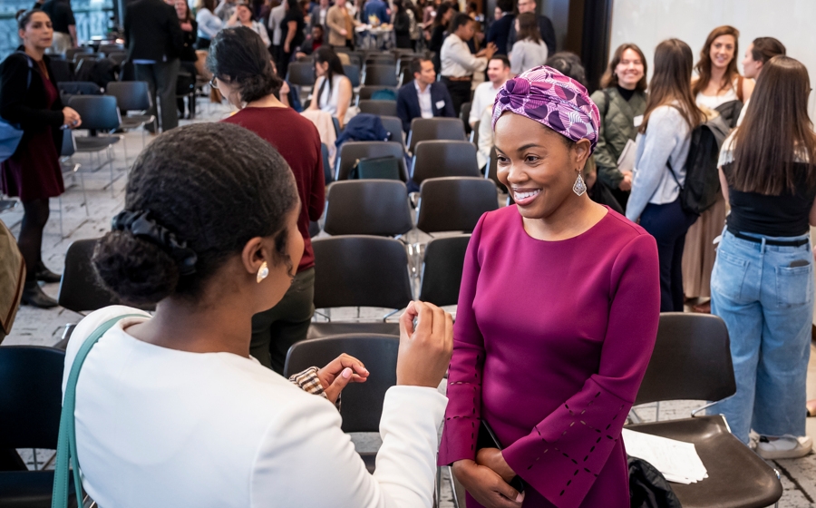 A woman wearing a purple dress smiles at an audience member as they speak.