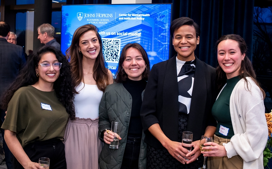 Five members of event crowd stand and smile at the camera.