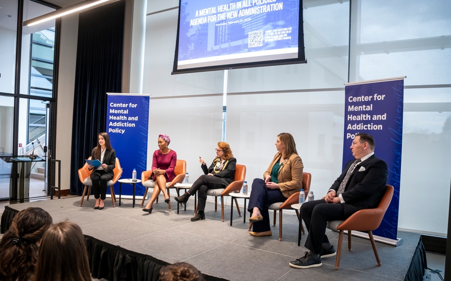 Five adults in business attire are seated on a stage. There is a banner that reads Center for Mental Health and Addiction Policy behind them.
