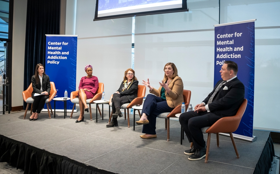 Five adults in business attire are seated on a stage. There is a banner that reads Center for Mental Health and Addiction Policy behind them.