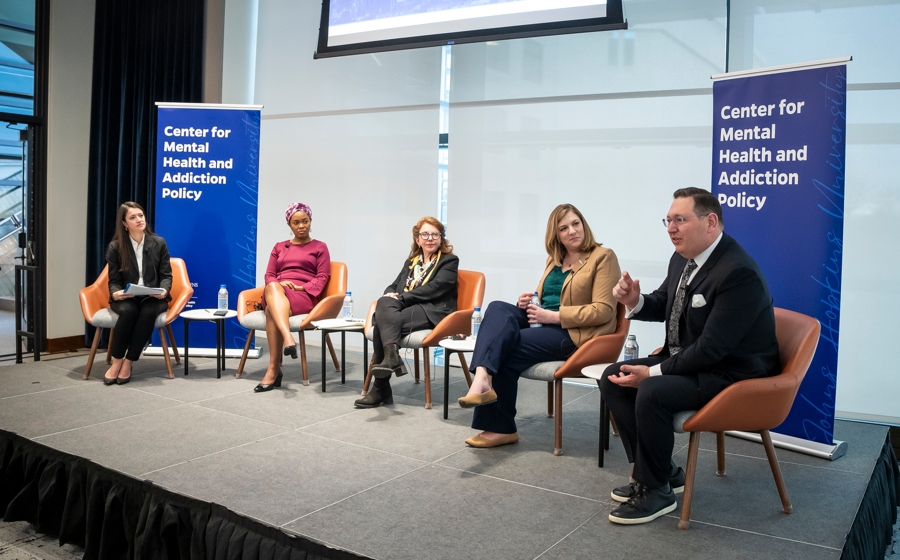 Five adults in business attire are seated on a stage. There is a banner that reads Center for Mental Health and Addiction Policy behind them.