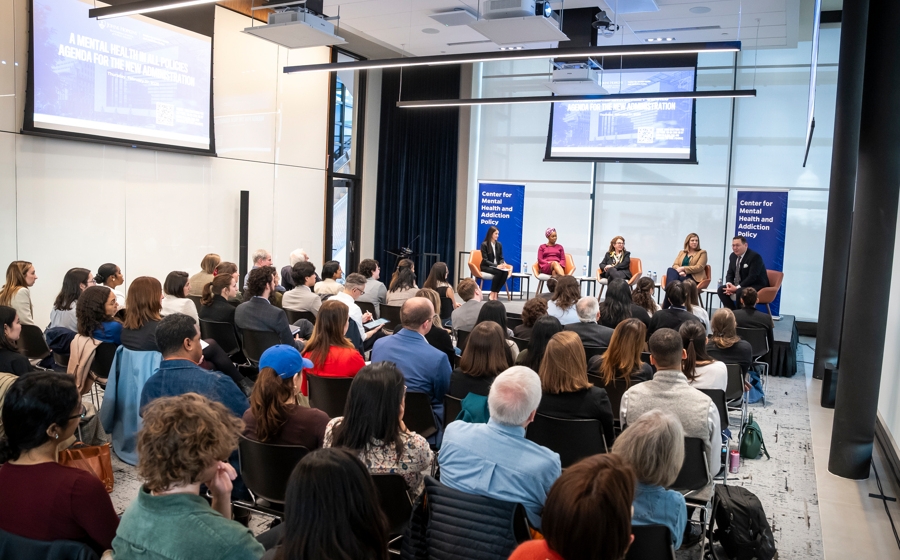 A crowd of over one hundreds people are seated in rows facing the stage.